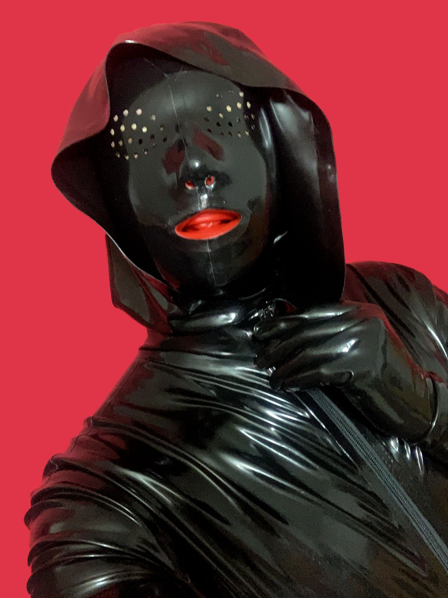 Alex Látex con máscara de látex con algunos hoyos en la parte de los ojos, tubos internos de nariz y boca de látex roja, con gorro de látex, fondo rojo